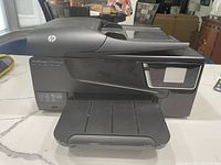 HP OfficeJet 6700 Premium all-in-one printer on countertop, showing paper tray and scanner section, no power cord visible