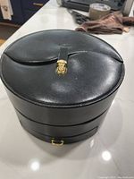 Closed black leather round jewelry box with gold clasp on a surface