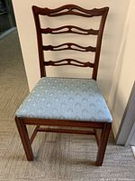 Single vintage wooden dining chair showing ladder back design with four curved horizontal slats and blue patterned upholstered seat.