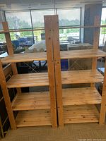 Two wooden shelving units placed side by side against a window with sunlight illuminating the natural wood. Each unit has four shelves and a simple sturdy construction.