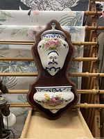 View of the entire ceramic wall fountain mounted on a wooden board with floral decoration and sculpted face.