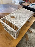 Side angle showing the woven herringbone top and open slatted side compartments of the white rattan breakfast in bed table with cup holder.