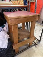 Wooden butcher block work table with pink top shown from an angle, displaying its legs, lower shelf, and surface.