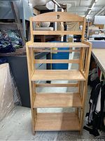 Wooden shelf unit standing upright showing 4 shelves and backrest with handle cutout
