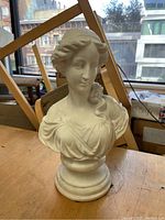 Cream colored female bust sculpture shown from front on wooden surface