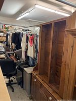 Wide view of wooden dining room cabinet in a cluttered room, showing tall upper shelving and part of furniture surroundings.