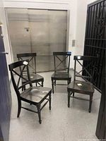 Four black wooden dining chairs arranged in a semi-circle, showing general wear and damage.