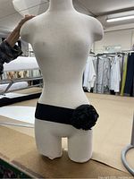 On mannequin showing black elastic belt with a large black fabric flower in front.