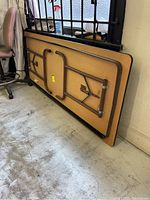 Folded rectangular table showing metal legs and frame against the underside, with a particleboard core surface and plastic leg caps.