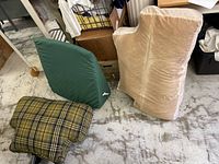 Three cushions on floor: green cushion, large beige plush cushion, yellow plaid notch-shaped cushion