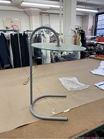 Side view of the round glass nightstand showing curved metal arm and U-shaped base.