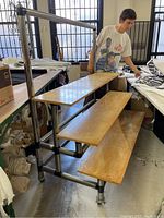 Side angle view of three-tier shelf unit showing the wooden shelves and tubular metal frame, with person nearby providing size scale.