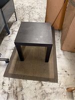 Side table on top of rectangular woven rug with brown border, viewed from a side angle.