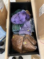 Box containing multiple plastic-packaged tie-dye shorts in colors such as purple, green, and brown, showing quantity and packaging condition.
