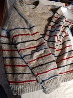 Photo showing two wool sweaters with beige base and multi-colored horizontal stripes laid flat.