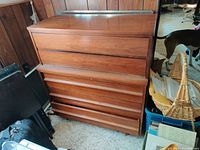 Front view of 5-drawer wooden dresser against wood-paneled wall with assorted items around
