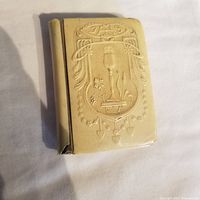 Front cover of small antique Bakelite-clad book with embossed religious symbols.