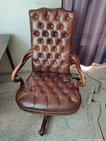 Front view of brown button-tufted leather chair with wooden arms and brass nailhead trim