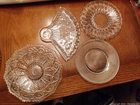 Four assorted decorative crystal patterned plates of various shapes and etched designs on wooden surface.