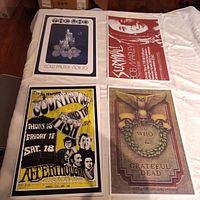 Top-down image of four colorful reprint posters laid out on a white sheet. Each poster represents classic rock artists and concerts including The Who & Grateful Dead, Bob Marley, Country Joe & The Fish, and the Tee Pee show at Cow Palace.