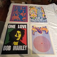 Four classic rock reprint posters laid flat on table: Big Brother and The Holding Company, Paisley Rain, Bob Marley, Country Joe & The Fish