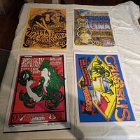Four classic rock band poster reprints laid out in a 2x2 grid on a white cloth, showing Velvet Underground, Puff of Kief, Big Brother and the Holding Company, and Canablis posters.