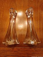 Photo of two clear crystal candlesticks on a wooden surface showing their tapered design and flared base.