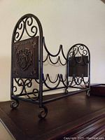 Front angled photo of a black metal eight bottle wine rack with scrollwork sides and decorative emblem plaque