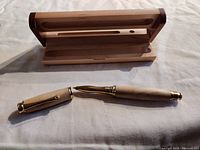 Photo showing the hand made maple wood pen with brass-colored accents placed next to its matching wooden storage case on a fabric surface.