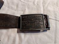 Photo shows a vintage Levi Strauss & Co men's belt with solid brass rectangular buckle embossed with brand logo and design, attached to a worn brown leather belt.