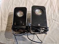 Photo showing the front of two black Logitech computer speakers with wired connections and volume control.