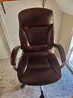 Front view of a brown leather office chair showing padded seat, backrest, and armrests on a metal base with caster wheels.