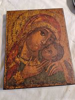 Photo of a wooden religious icon panel showing Mary holding baby Jesus in traditional style with cracked aged paint.