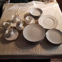 Overhead view of multiple bone china pieces including stacks of plates, bowls, teacups with saucers and creamers on a cloth