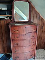 Tallboy dresser showing all five drawers with brass handles and attached large mirror with curved edges.
