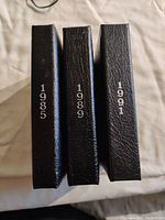 Three black presentation cases side by side with years 1985, 1989, 1991 printed on spine.