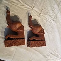Pair of wooden elephant bookends shown from side angle on white fabric background, highlighting the carved elephant shapes and bases.