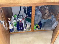 Photo of multiple cleaning products stored under a kitchen sink with wooden cabinet frame visible.