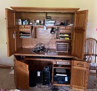 Front view of the oak wood computer desk with hutch, upper cabinets with doors open showing shelves and small drawers, desk surface with cables, revealing internal compartments with computer tower and printer below.