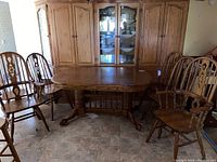 Dining table with two leafs surrounded by four high back chairs and two captain chairs, medium-tone wood, traditional style.