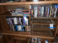 Full view of wood shelving with stacked CDs and DVDs, some in a black carrying case.