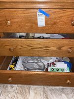 Three wooden drawers, two open showing partial contents including glass dish, flatware trays, and hardware items.