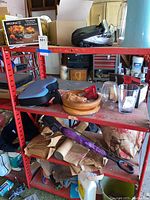 Four red metal shelves holding various household items including bags, a travel pillow, umbrella, glass cups, and wooden bowl with dessert dishes.