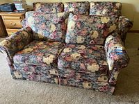 Full view of the floral fabric love seat showing two cushions, armrests, and the overall pattern and condition.