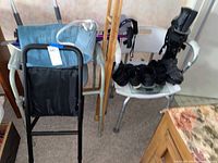 Photo showing black orthopedic shoe with multiple straps placed on white shower chair seat along with other black shoes, aluminum crutches, and heating pad hanging on walker.