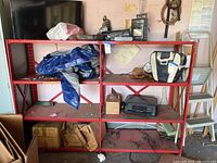 Full view of red metal shelves with assorted items including power tools, a tarp, carrying bag, and cardboard boxes.