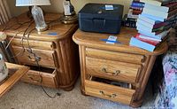 Two matching wooden side tables with items on top and one drawer open showing interior.