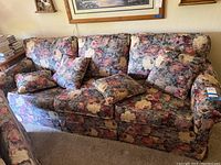 Full view of floral fabric sofa with multiple loose cushions showing overall floral pattern and condition including wear and pet damage.