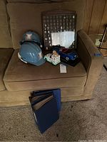 Overview of thimble collection in wooden display case, two blue Hoover Dam helmets, and two decorative model cars on a brown couch.
