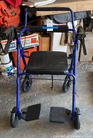 Front view of blue walker with padded seat, hand brakes, and footrests.